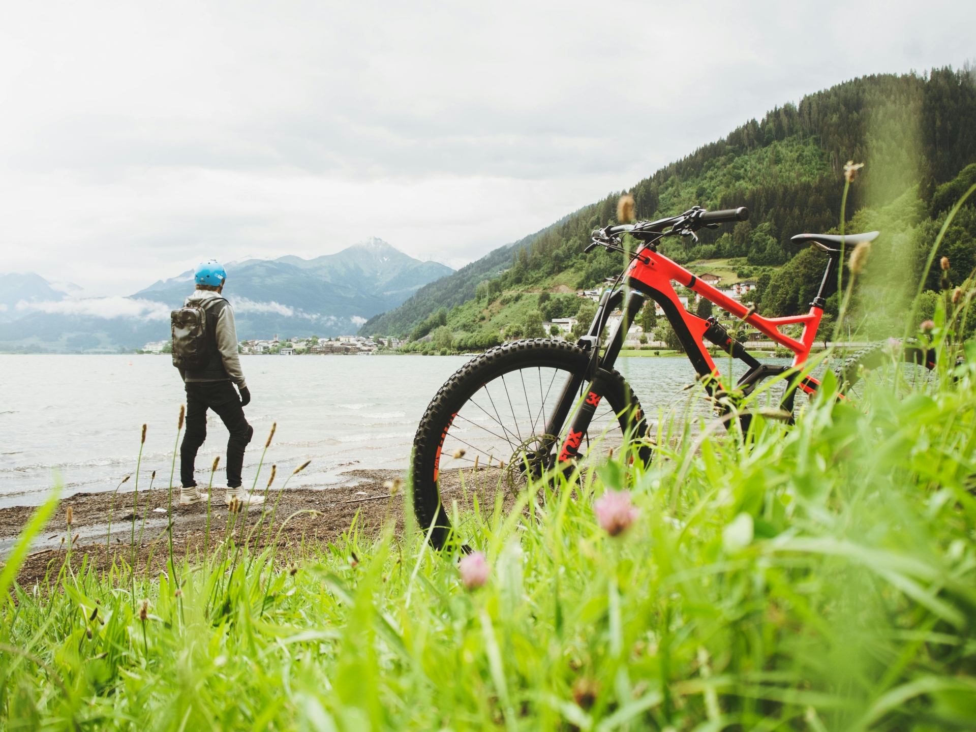 Fahrradfahrer vor einem Panorama mit See und Bergen. Sein Mountainbike steht im Vordergrund des Bildes.