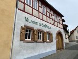 Museum an der Münze Neuleiningen Fachwerkhaus mit weißen Wänden, braunen Fensterläden und grünem Schriftzug 'Museum an der Münze' über drei Fenstern.