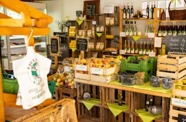 Regal mit regionalen Produkten wie Äpfeln, Trauben, Flaschen mit Saft oder Wein und Tüten in einem Hofladen.